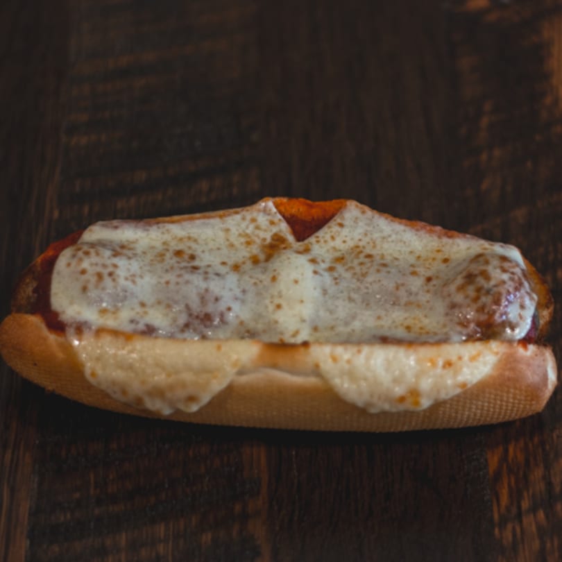 Mane Course Sandwiches' meatball sub, topped with melted mozzarella cheese and marinara sauce on a wooden table.