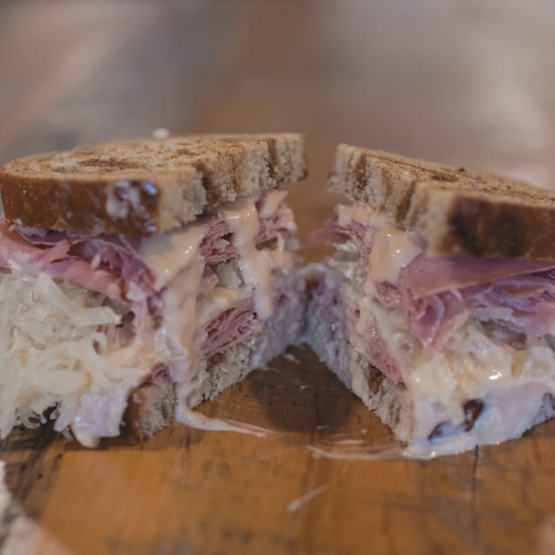 A Mane Course sandwich, cut in half, revealing layers of meat, sauerkraut, and creamy sauce.