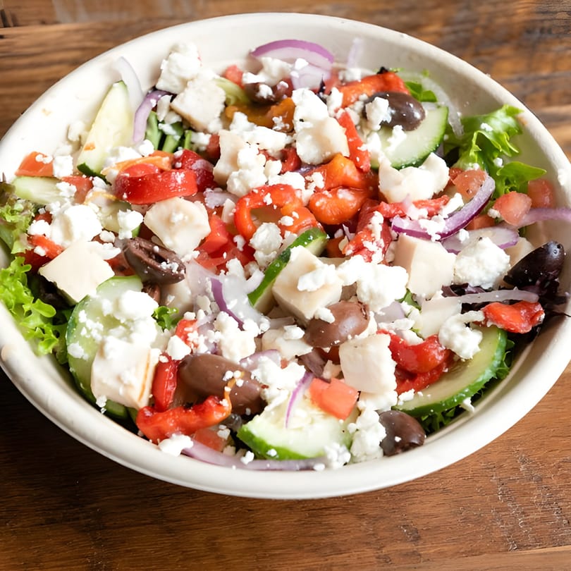 A vibrant Greek salad with lettuce, cucumbers, tomatoes, red onion, olives, and feta cheese.