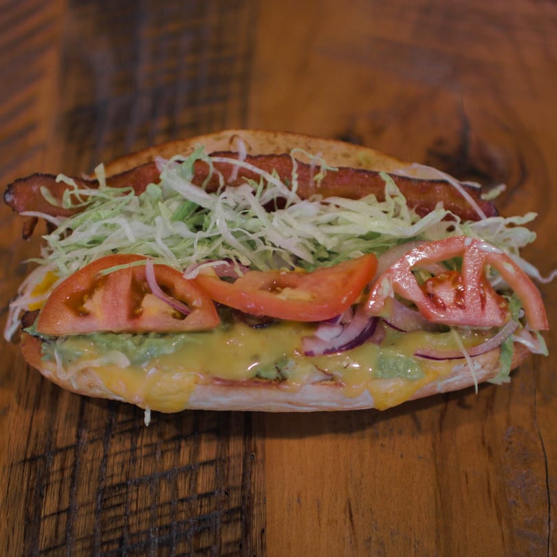 A Mane Course sandwich with bacon, shredded lettuce, tomatoes, red onion, guacamole, and melted cheese.