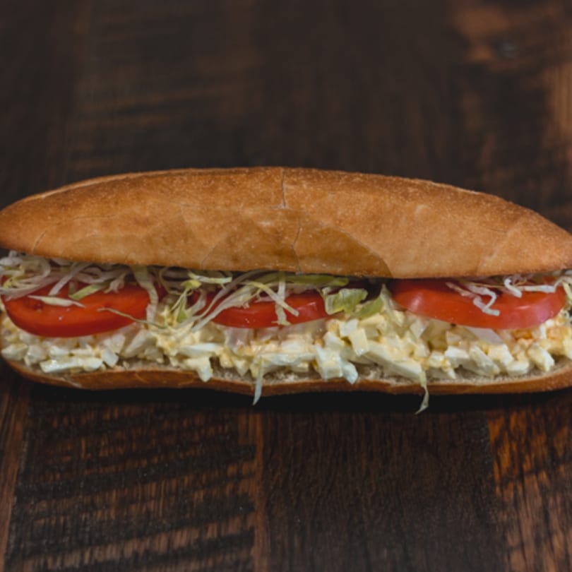 Mane Course Sandwiches' egg salad sub with tomatoes and shredded lettuce on a wooden table.