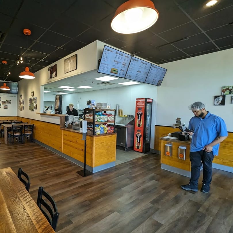 Interior of Mane Course Sandwiches, showing the counter, menu boards, and dining area with tables.