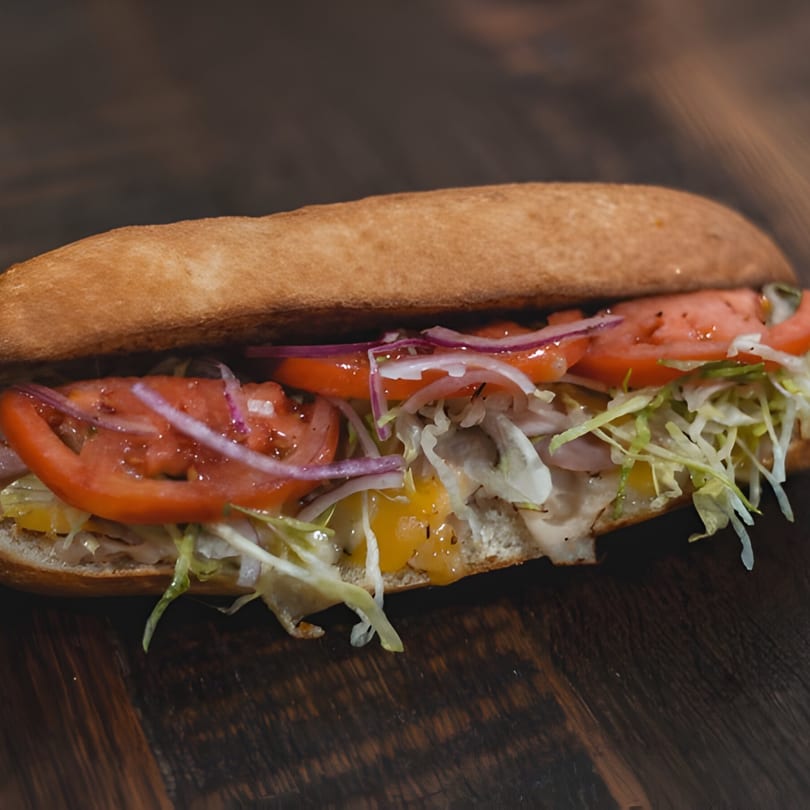 Mane Course Sandwiches' sub sandwich with tomatoes, red onions, lettuce, and cheese on a wooden table.